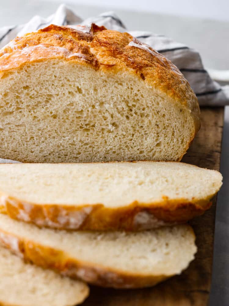 A cut loaf of potato bread on a rustic cutting board. A striped kitchen towel is next the the loaf of bread.