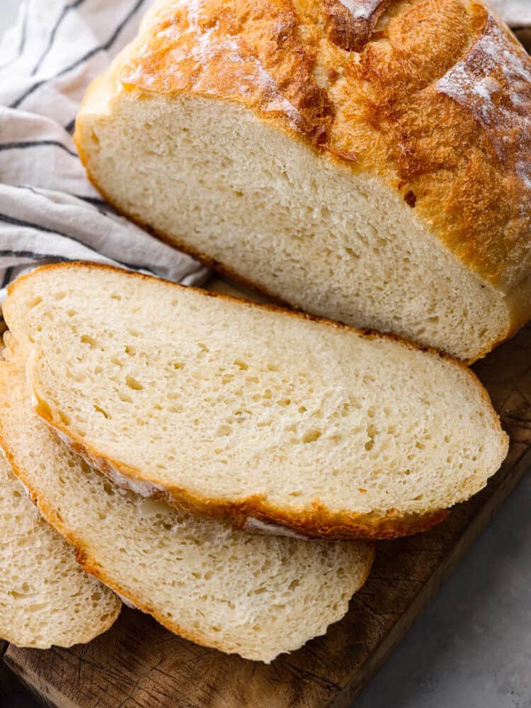 Close up view of sliced pieces of bread on a rustic brown cutting board. Half of the loaf is sliced, and the other half of the loaf is still whole.