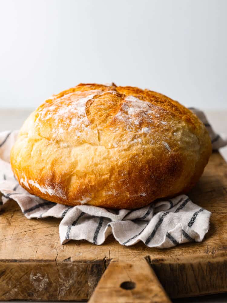 Side view of a loaf of potato bread on top of a striped kitchen towel and rustic cutting board.