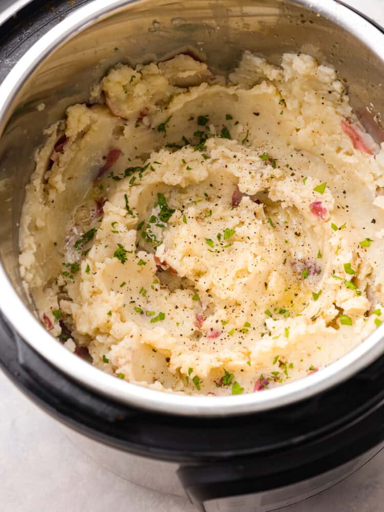 Mashed potatoes in an Instant Pot, seasoned with herbs.