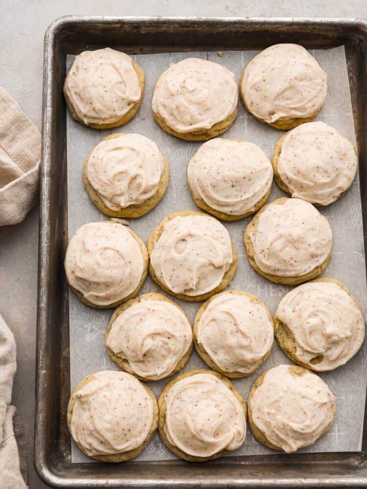 Frosted Sugar cookies sitting on parchment on a baking sheet.