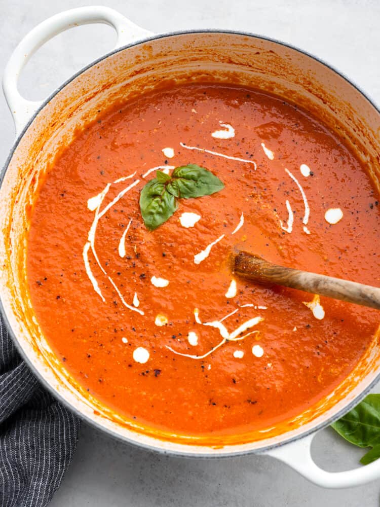 Top-down view of tomato basil soup in a blue pot, garnished with herbs and a dollop of cream.