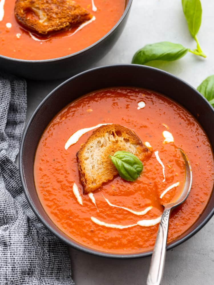 Top-down view of tomato basil soup, drizzled with cream and served with bread.