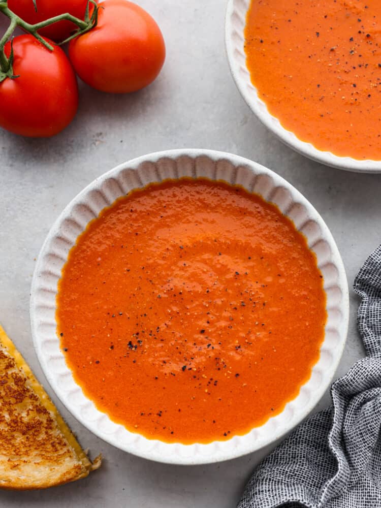 Two bowls of tomato soup with tomatoes off to the side.