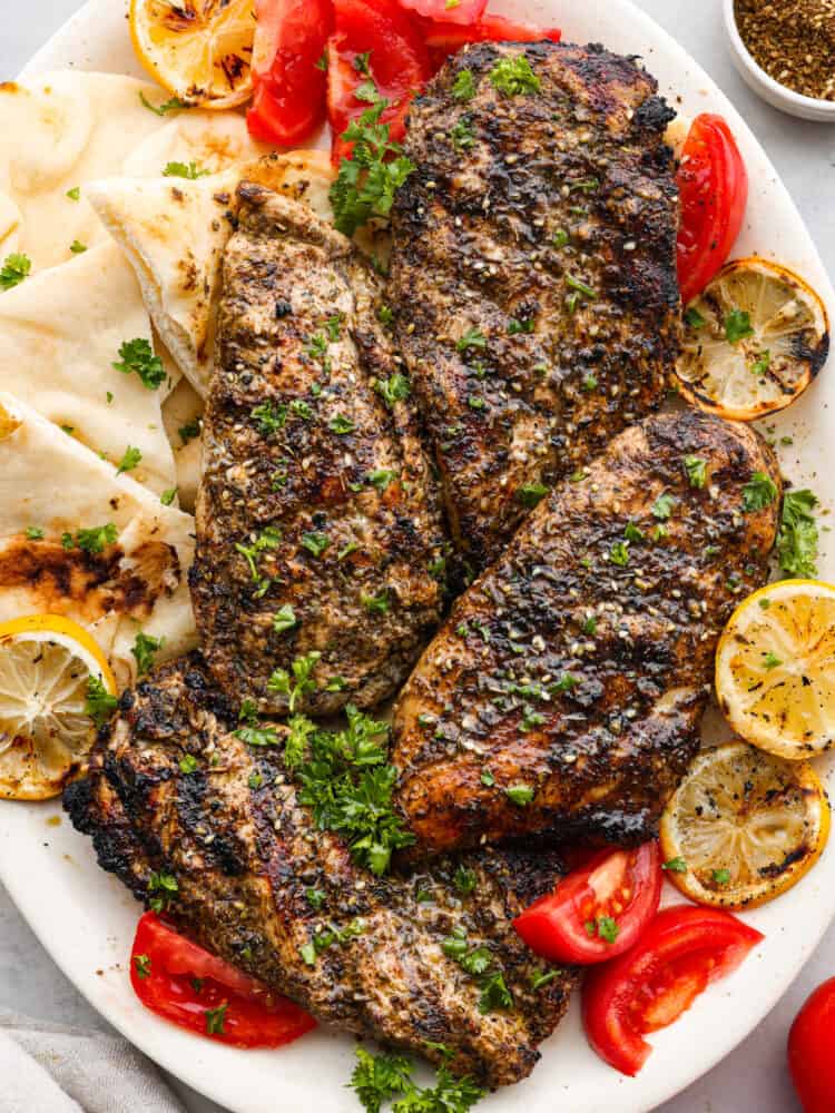 Grilled chicken on a plate with pita bread, lemons, and tomatoes.