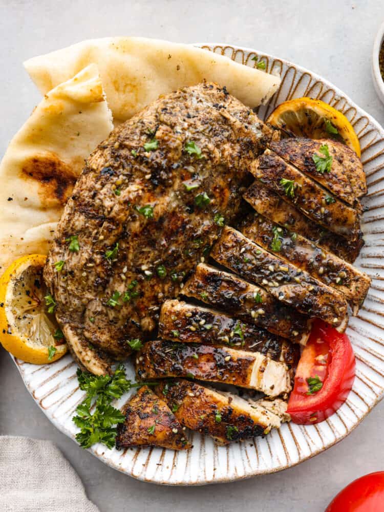 Za'atar chicken on a plate cut up with pita bread, tomatoes, and lemons.