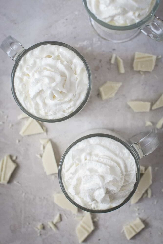The top view of some white hot chocolate in glass cups with whipped cream on top. 