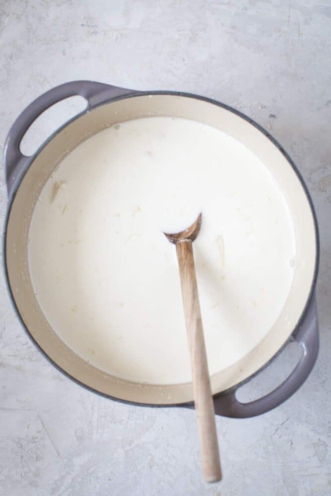 Chocolate caliente blanco en una olla con una cuchara de madera. 