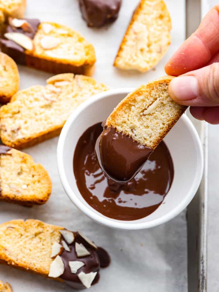 A hand dipping the biscotti in chocolate.
