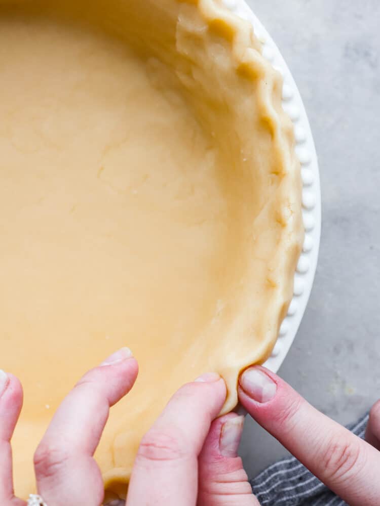 Close up of pie crust with hands crimping the edges.