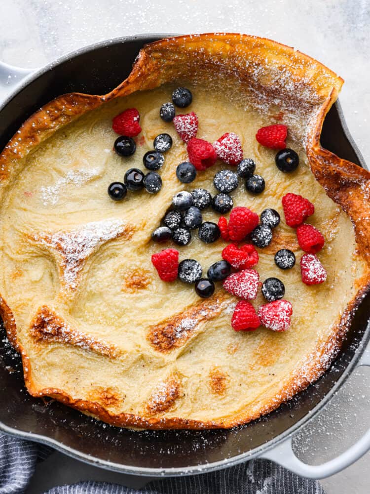 Top-down view of a Dutch baby in a cast iron skillet, garnished with powdered sugar and berries.