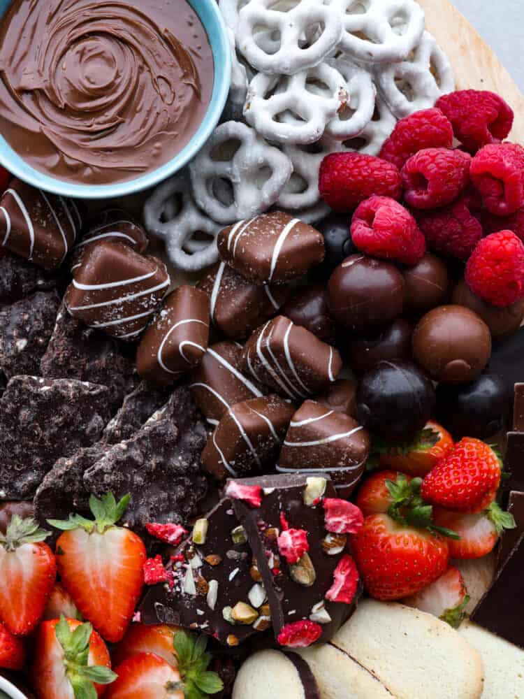 Top view of chocolate board with candy, pretzels, fruit, and a bowl of nutella.