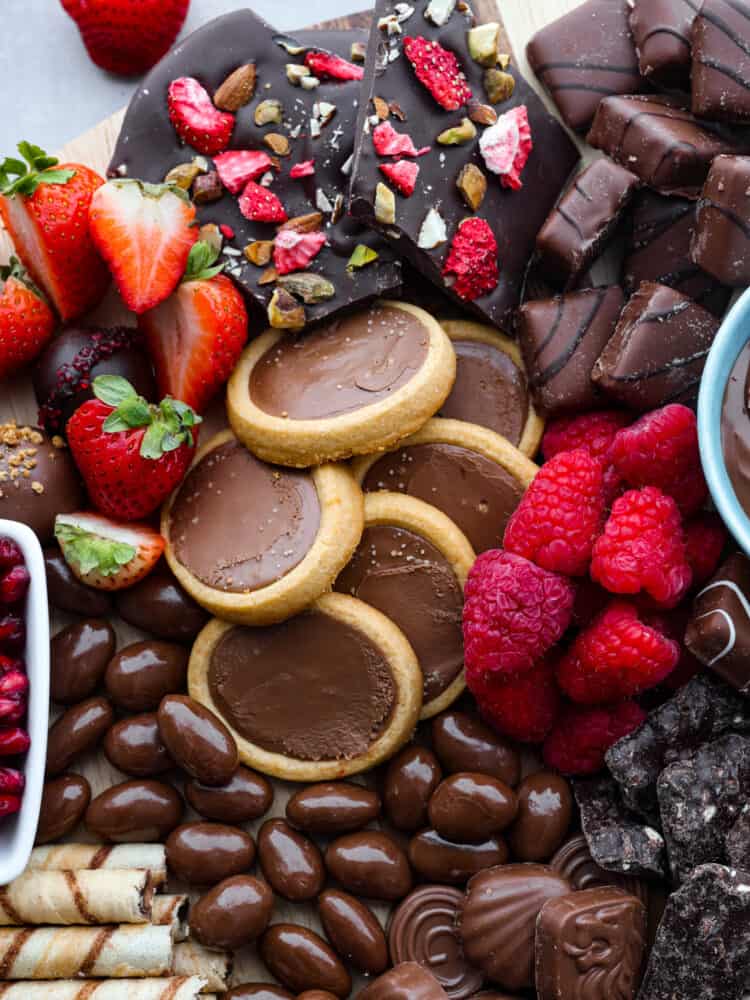 Close up photo of the chocolate charcuterie board. Cookies, chocolate almonds, and fruit are scattered on the board.