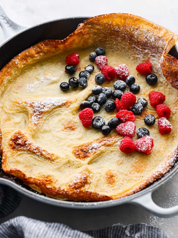 Hero image of a cooked Dutch baby topped with powdered sugar and berries.