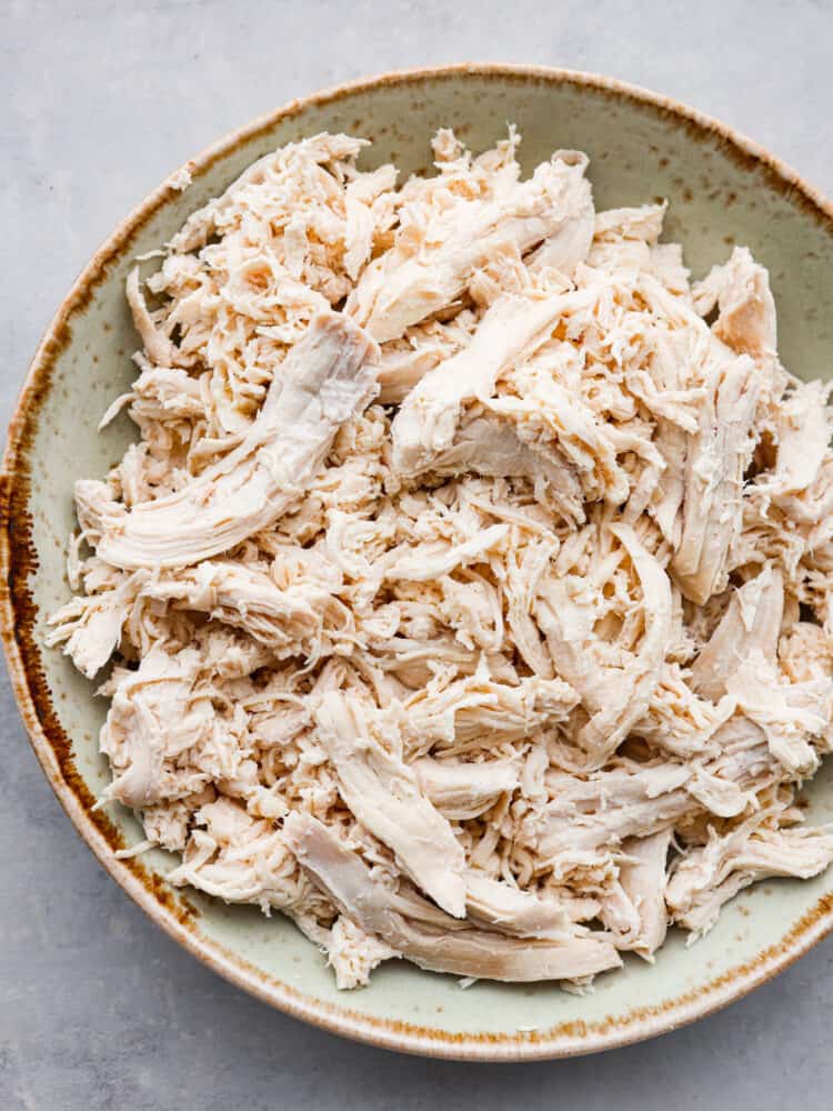 Close top view of shredded boiled chicken in a rustic green and brown bowl.