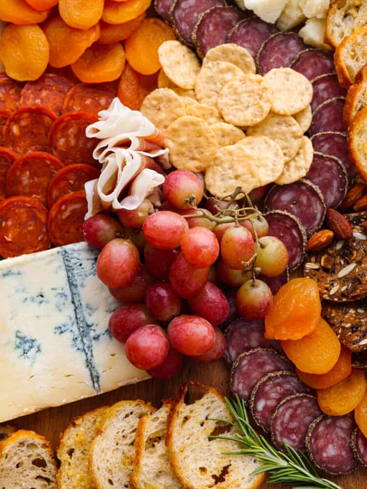 A close up of the Italian charcuterie board with grapes, mangoes, cheeses, and crackers.