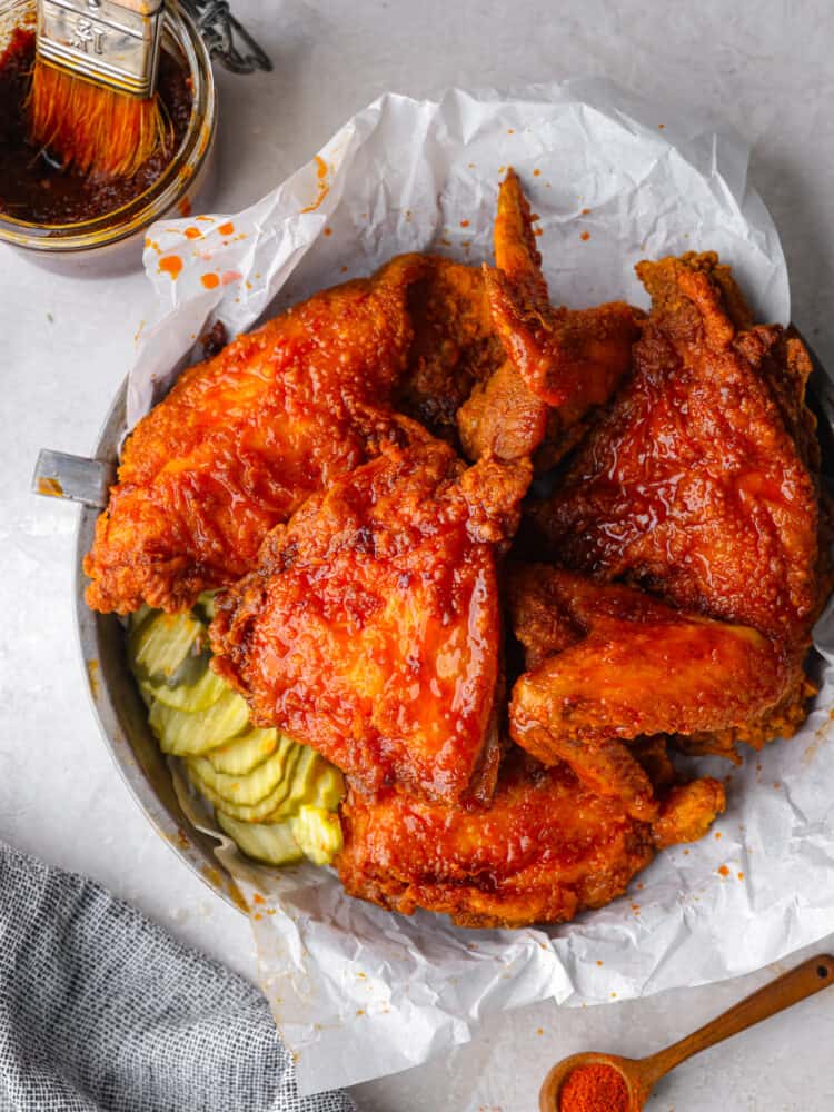 Nashville hot chicken on parchment on a plate with pickles next to it.