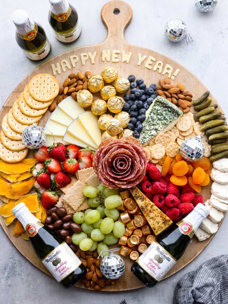 Overhead view of new year's charcuterie board. Miniature sparkling ciders and disco balls surround the board.