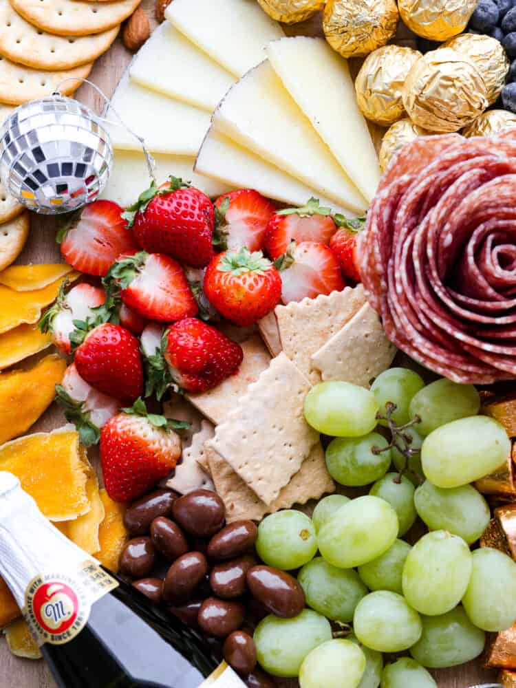 Close up view of fruit, crackers, cheese, and salami rose on charcuterie board.