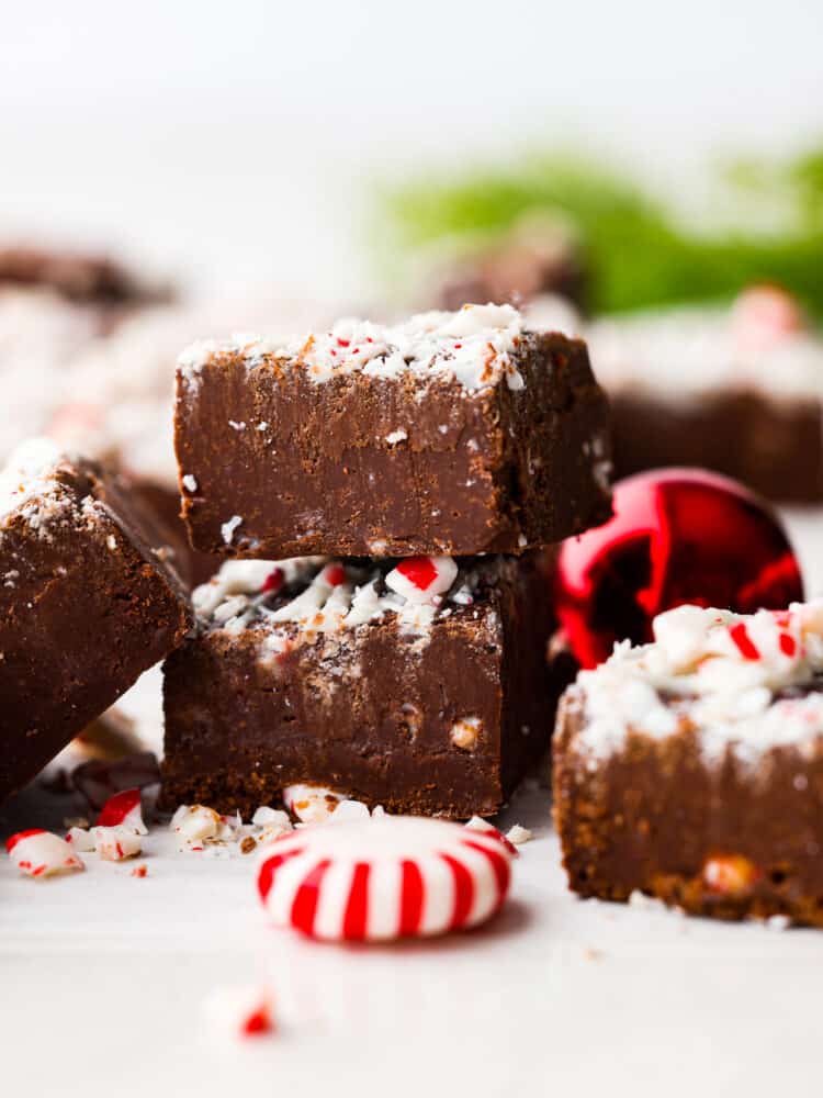 Chocolate peppermint fudge stacked on top of each other with red Christmas ornaments in the background.