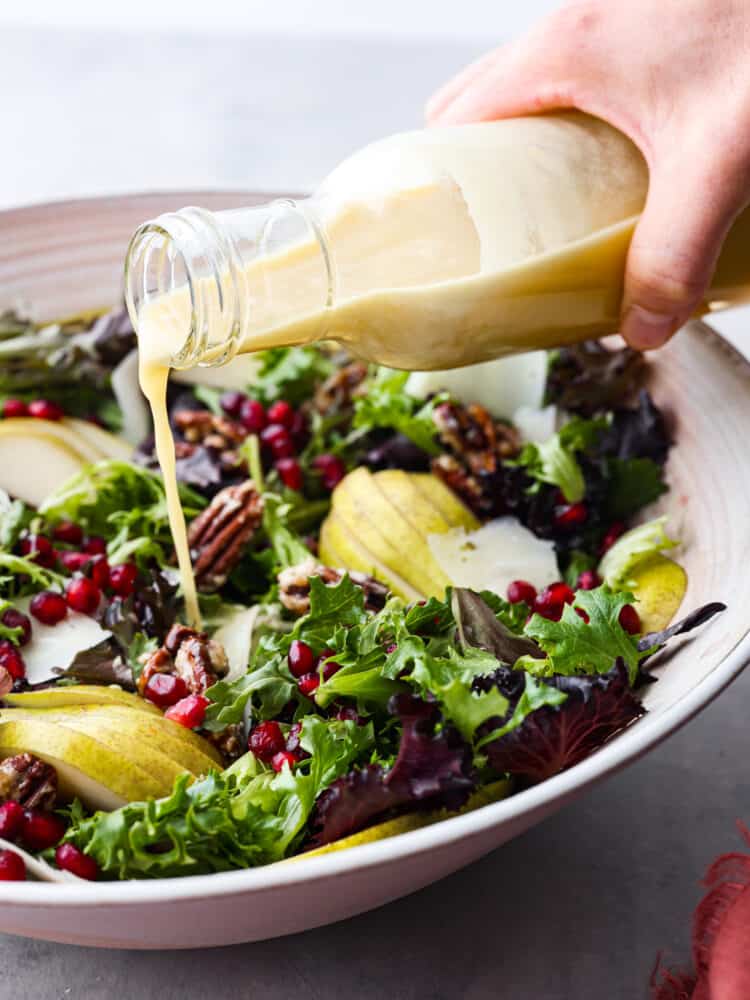 Champagne vinaigrette being poured over a salad with pomegranates and pears.