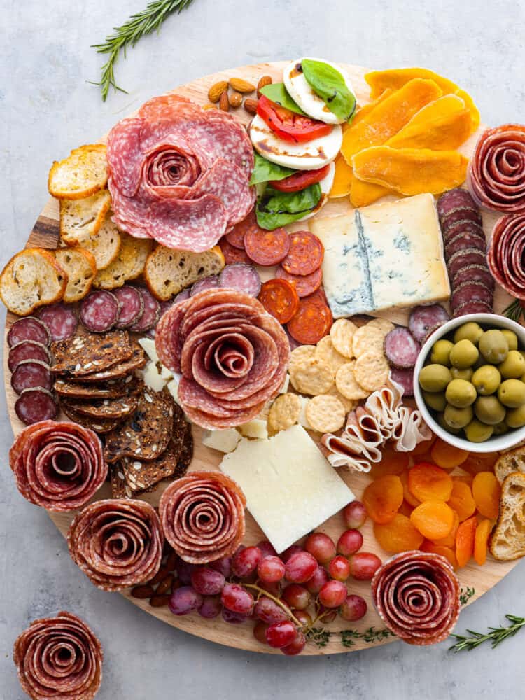 A charcuterie board with salami roses and an assortment of meats, cheeses, fruits and veggies.