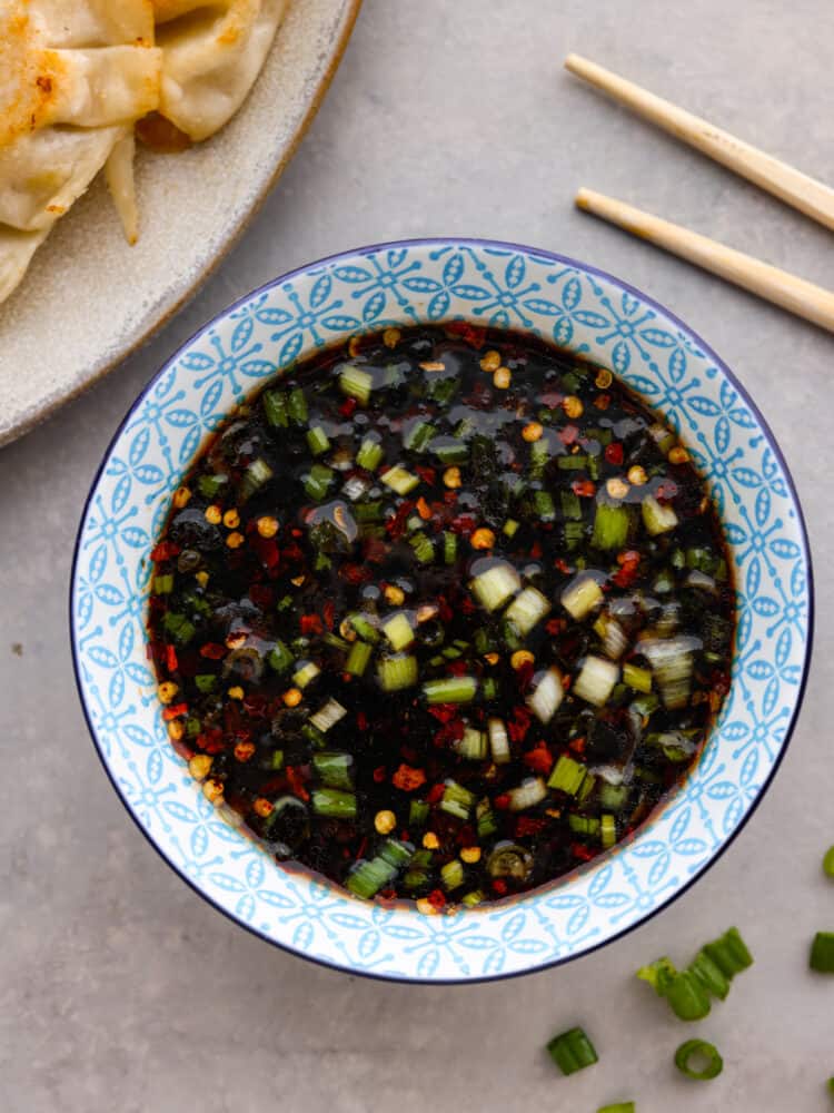 Top view of potsticker sauce in a blue patterned bowl. Chopsticks and a plate of potstickers are styled beside the bowl.