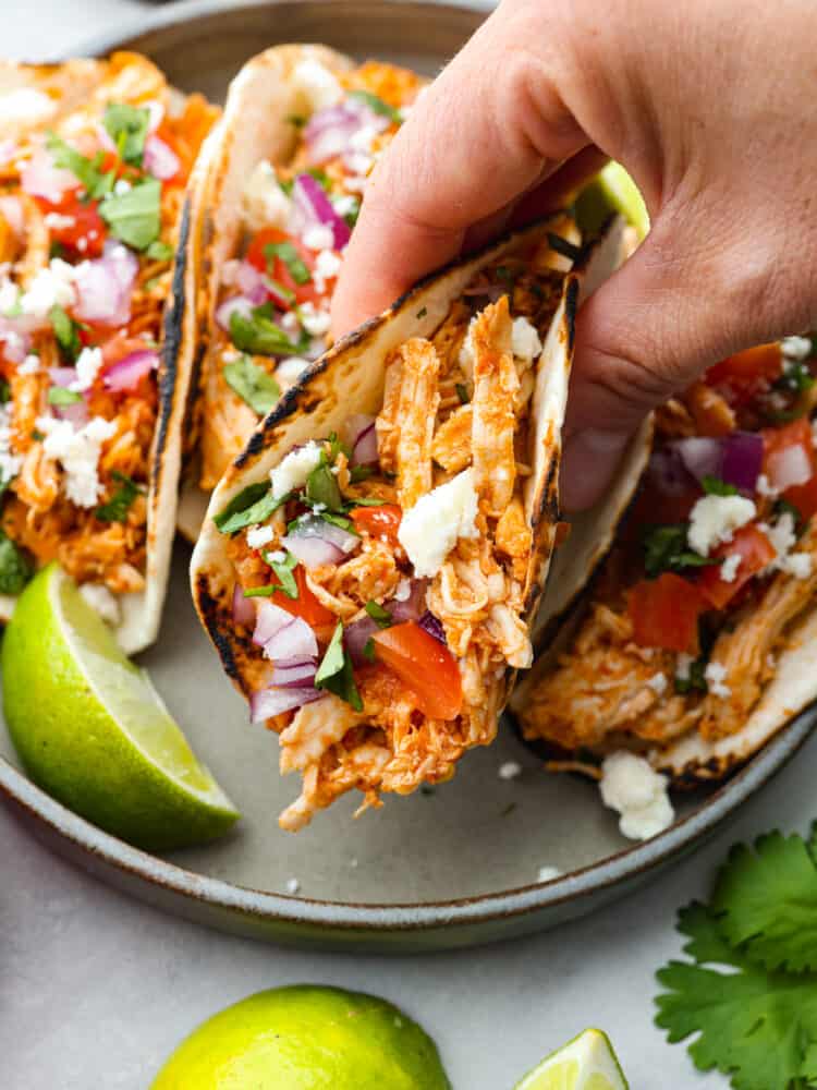 En hand som håller en taco över en tallrik med andra tacos.
