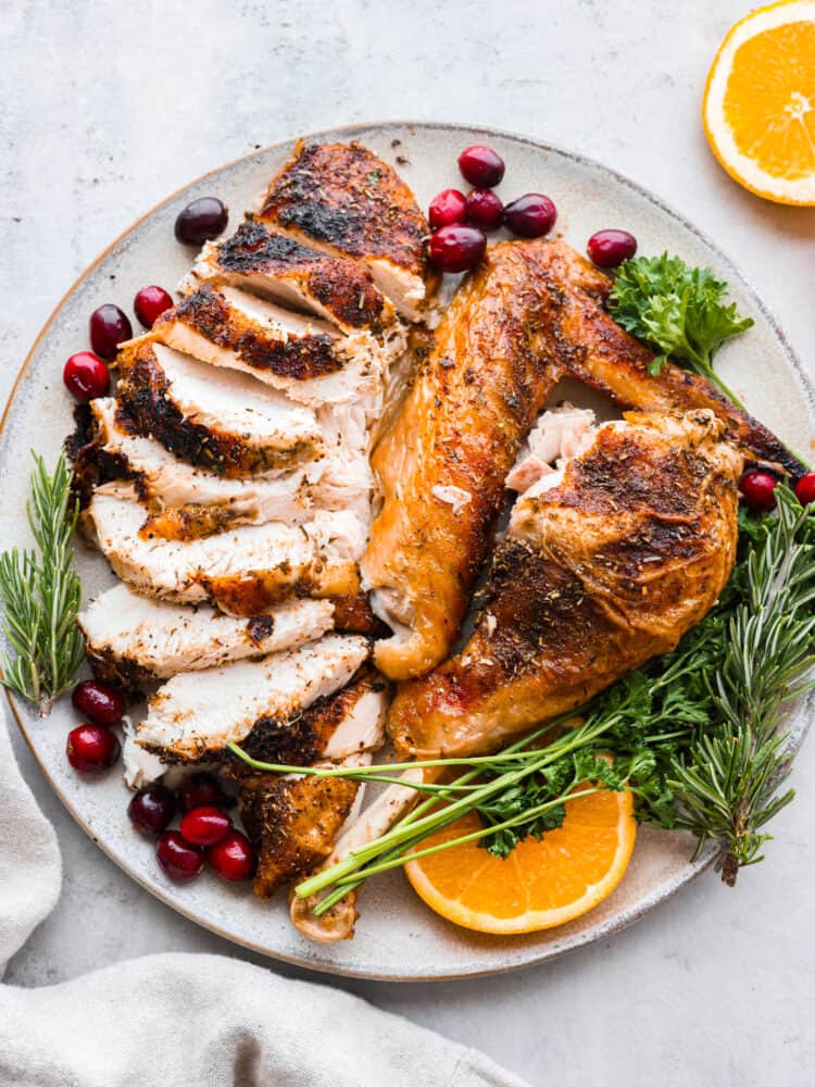 Turkey cut up and presented on a platter with oranges, cranberries, and fresh herbs.