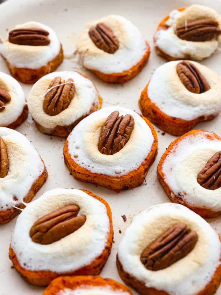Close up view of sweet potato bites on a large platter with melted marshmallows and a pecan on top.