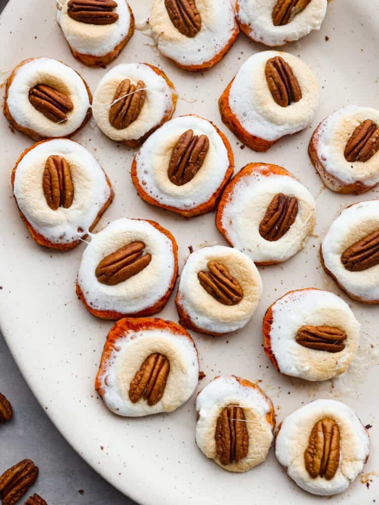 Top view of sweet potato bites on a large platter with melted marshmallows and a pecan on top. Pecans are scatted on the counter next to the platter.