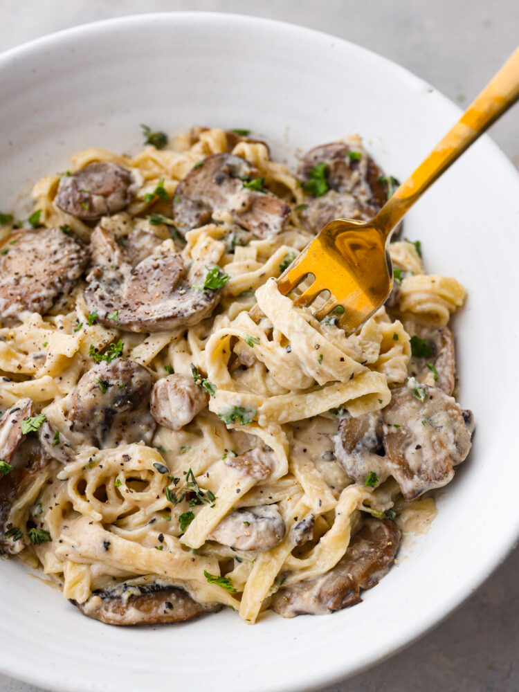 Tagliatelle pasta served with mushroom sauce. There is a bite being taken out with a gold fork.