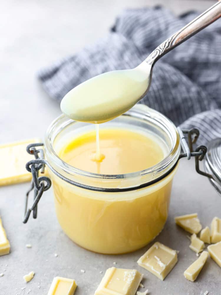 A spoon taking a scoop out of the sauce jar with white chocolate sprinkled around it.