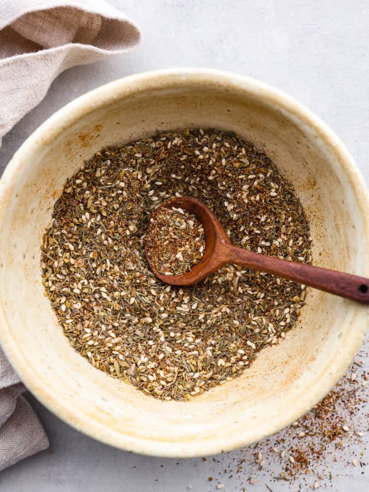 Za'atar seasoning in a white bowl with a wooden spoon in it.