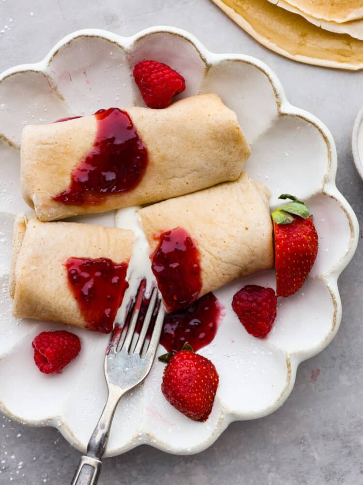 Cheese blintzes on a white plate with fresh berries and a fork cutting through the center.
