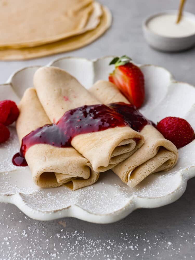 Blintzes stacked on a plate with strawberry jam on top.
