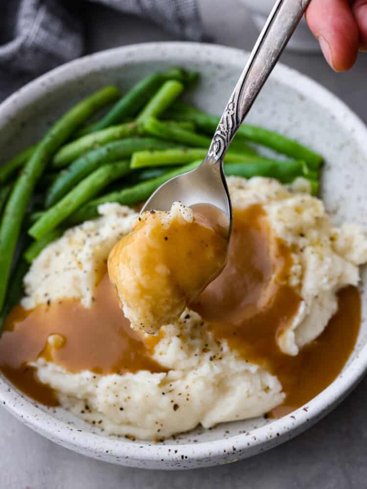 Brown gravy on top of mashed potatoes with a spoon taking a scoop out of it.