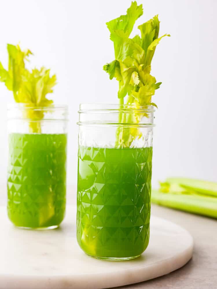 Two glasses of celery juice in mason jars. A leafy celery stalk is styled inside each glass of juice.