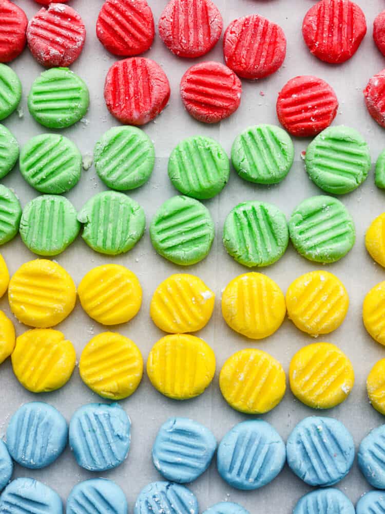 Cream cheese mints in red, green, yellow, and blue all lined up on a parchment paper.