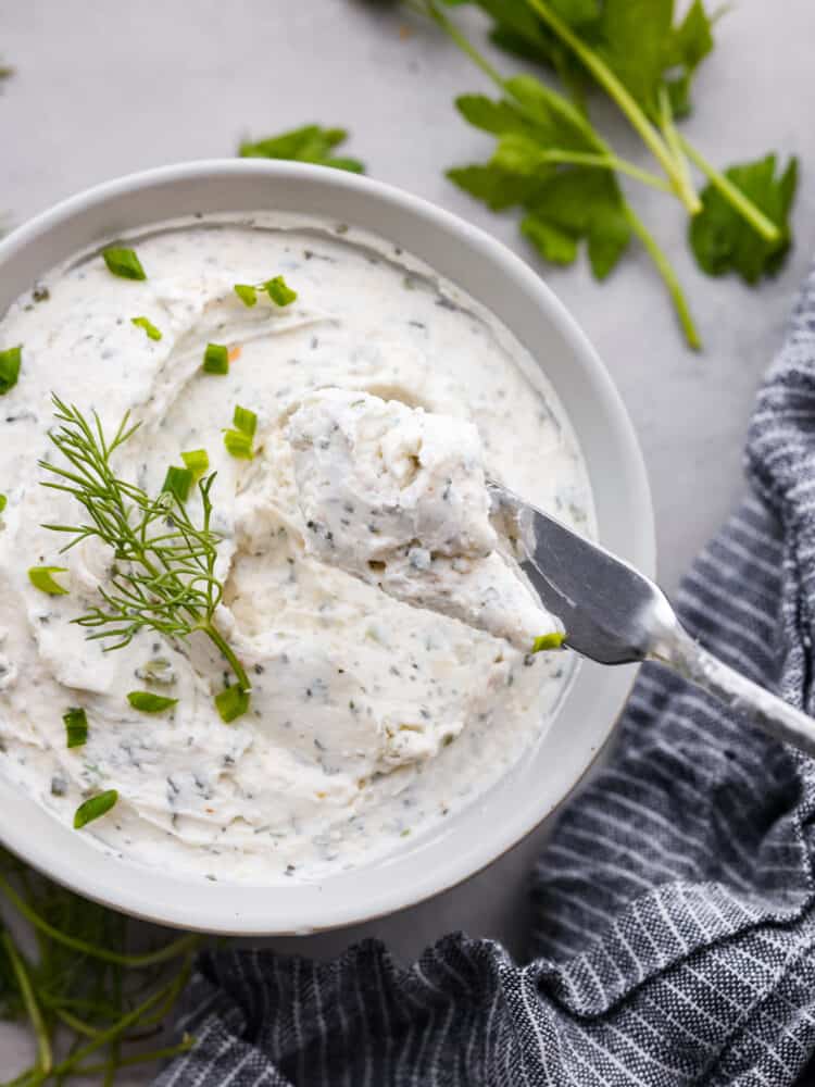 Garlic herb cream cheese spread on a butter knife with the bowl in the background.