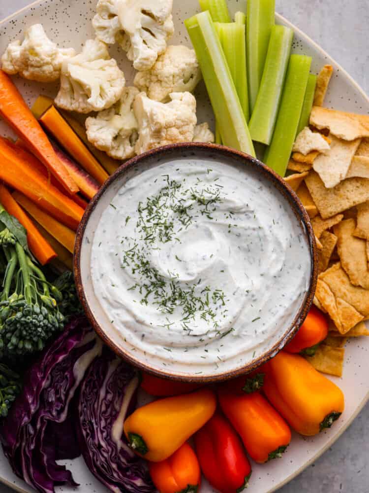 Top-down view of Greek yogurt dip served with baked crackers and fresh veggies.