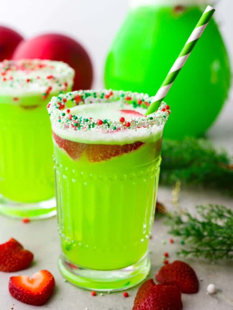 Hero image of Grinch punch in a glass garnished with sliced strawberries and holiday sprinkles.