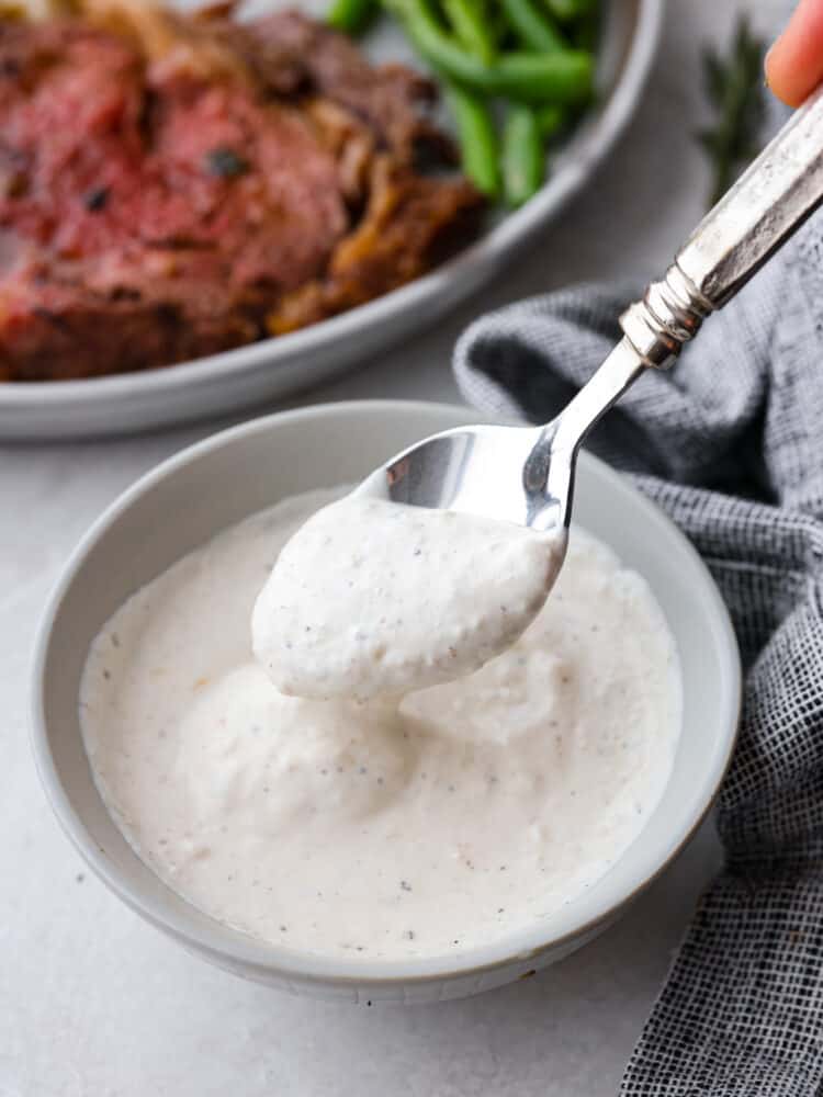 A picture of horseradish sauce on a spoon with a steak in the background.