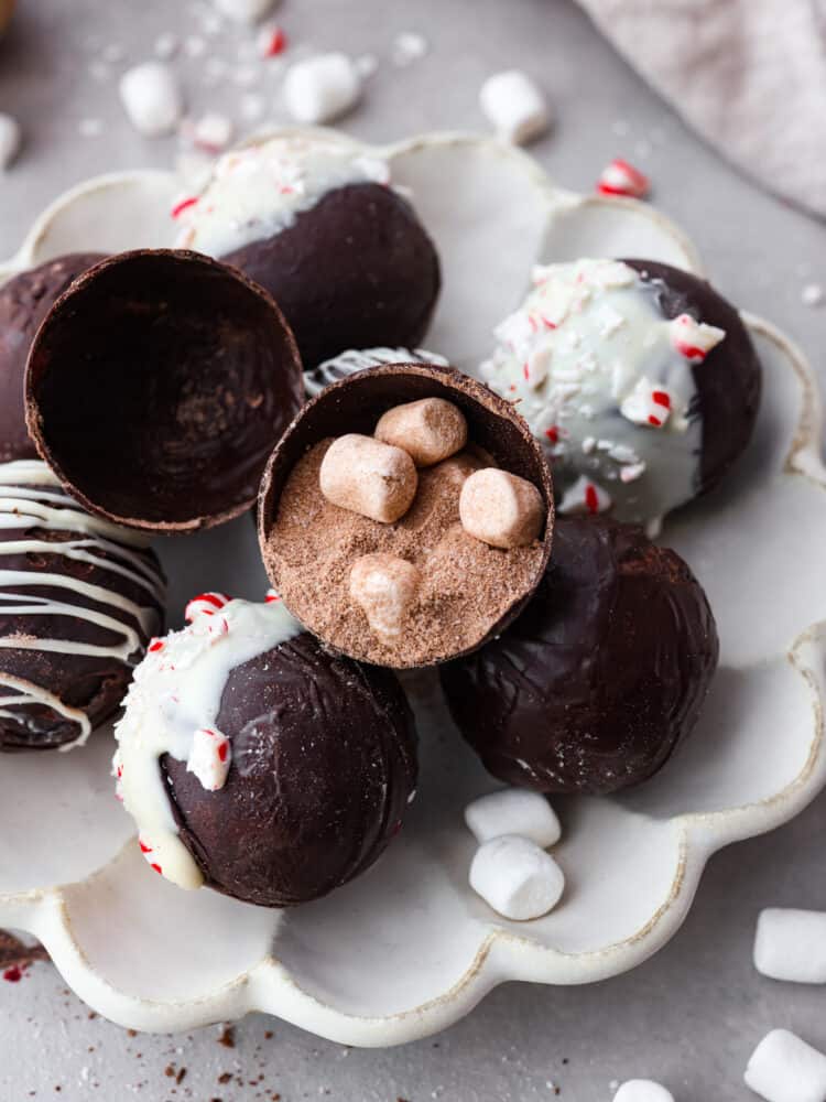 Hot chocolate bombs stacked on a serving dish. One is split in half so the cocoa powder and marshmallow filling can be seen.