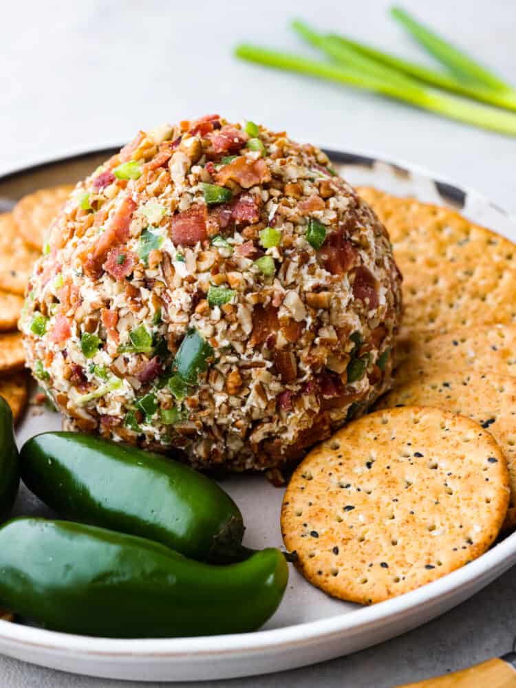 A whole cheese ball served on a white tray with crackers and whole jalapenos for decoration.