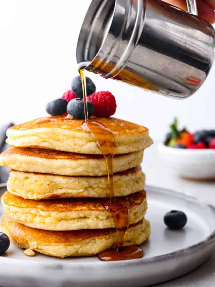 Syrup being poured over a stack of 5 pancakes.