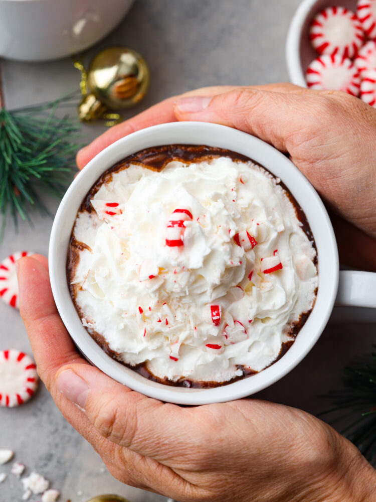 Top-down view of peppermint hot chocolate in a white mug, being held.