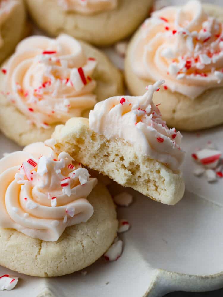 Close up view of peppermint meltaways with frosting and sprinkled peppermint candy on top. A bite is taken out of one of the cookies 