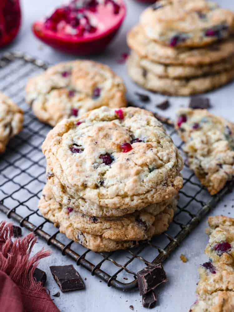 Pomegranate chocolate chunk cookies stacked on top of each other with cookies and pomegranate in the background.