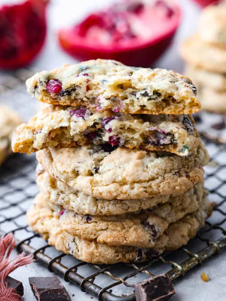 Pomegranate chocolate chunk cookies stacked on top of each other on a wire rack, one broken in half to show the inside.